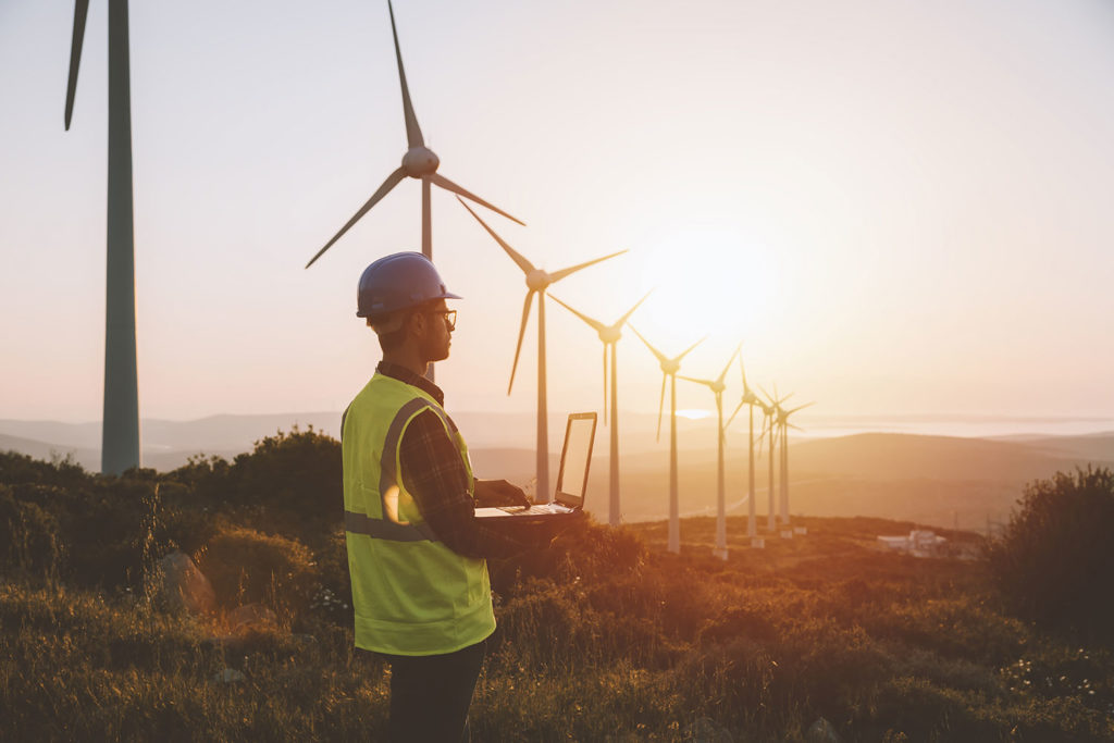 Worker stands near wind turbines and surveys data during sunrise
