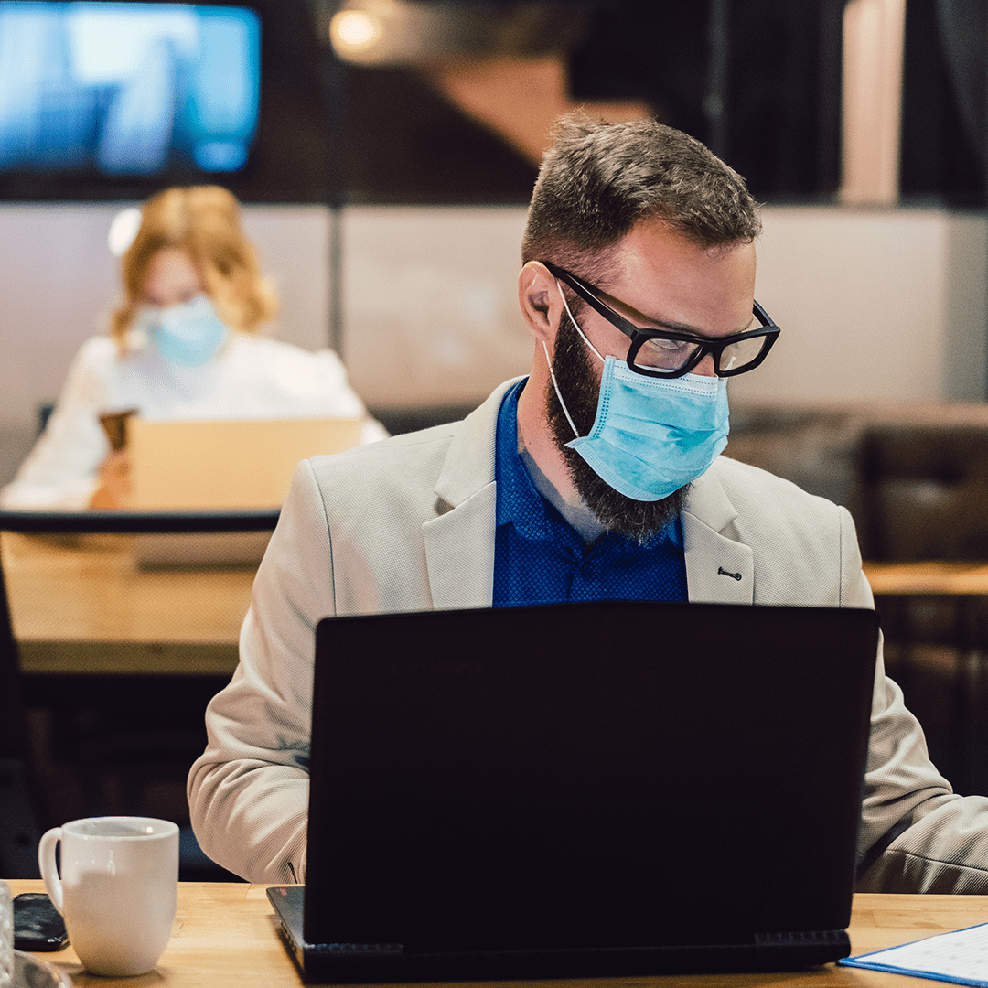 Employees sitting at desk in business attire working and wearing facemasks