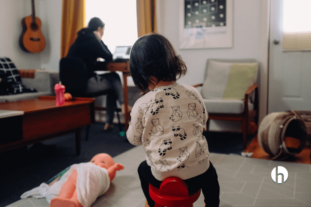 toddler with their back to the camera watches their mom work from her home office