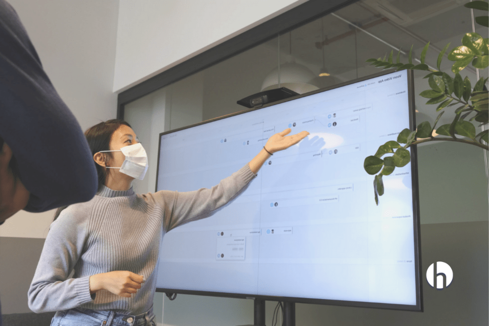Woman wearing a mask in the office presents on a whiteboard to staff