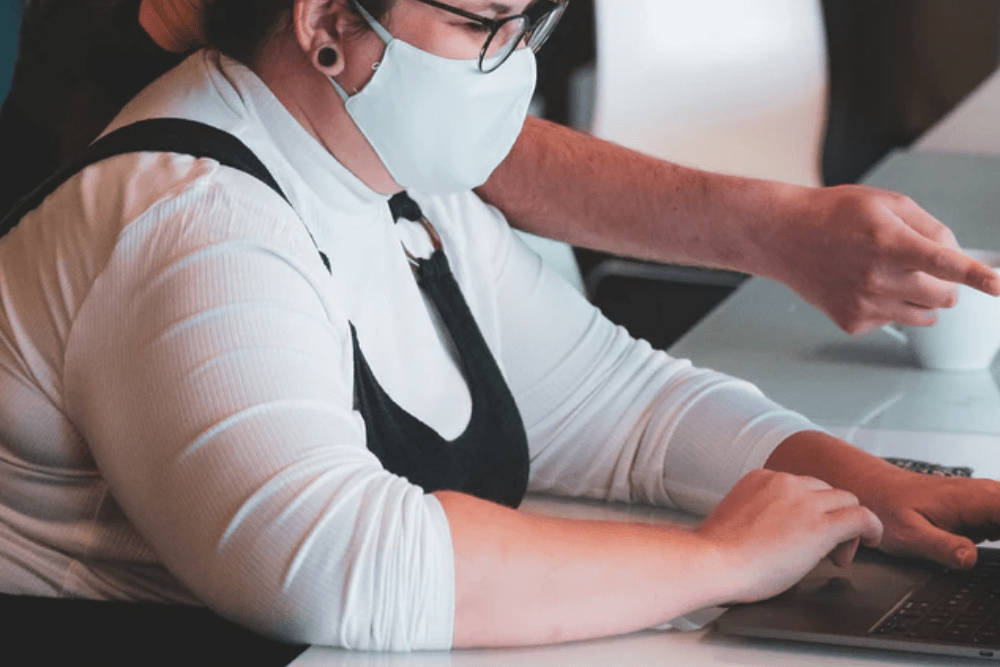Woman working at a laptop wearing a mask